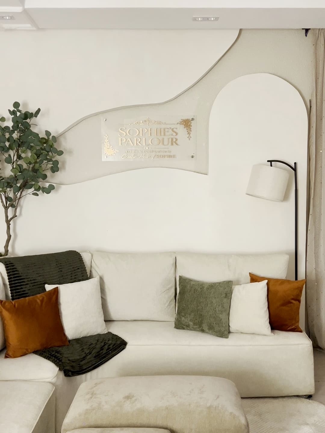 A cream sectional sofa with green and rust cushions beneath the Sophie's Parlour sign